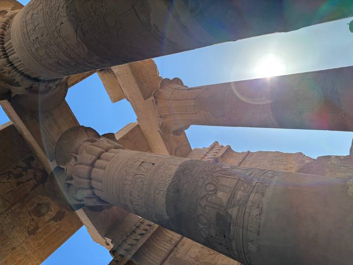 Sunlight streams past the carved stone columns of Kom Ombo Temple creating lens flare.