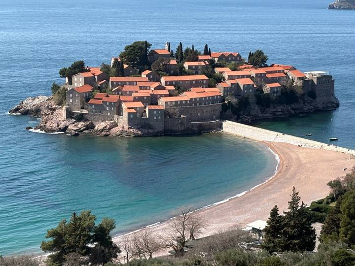 Iconic fortified island of Sveti Stefan jutting into turquoise Adriatic waters under clear skies.