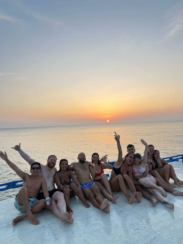 Cheerful group on a boat raising hands as the sun sets over calm sea.