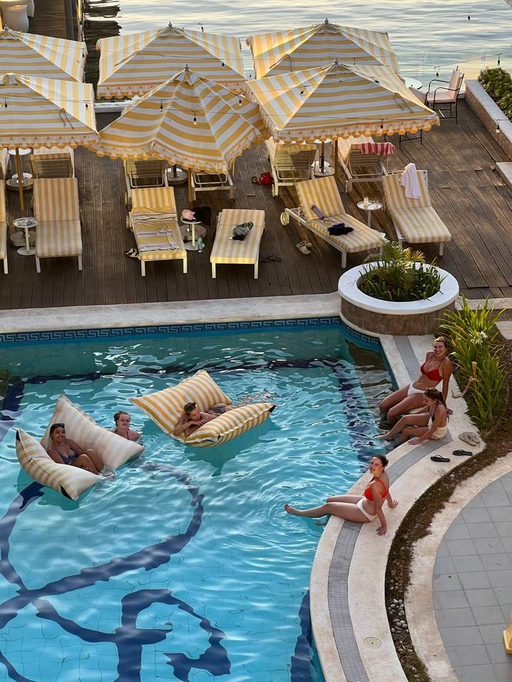 Guests lounging on striped floats and poolside chairs at a boutique hotel pool.