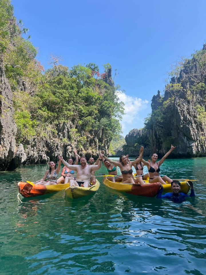 Large group paddling yellow kayaks through dramatic limestone cliffs on clear blue water.