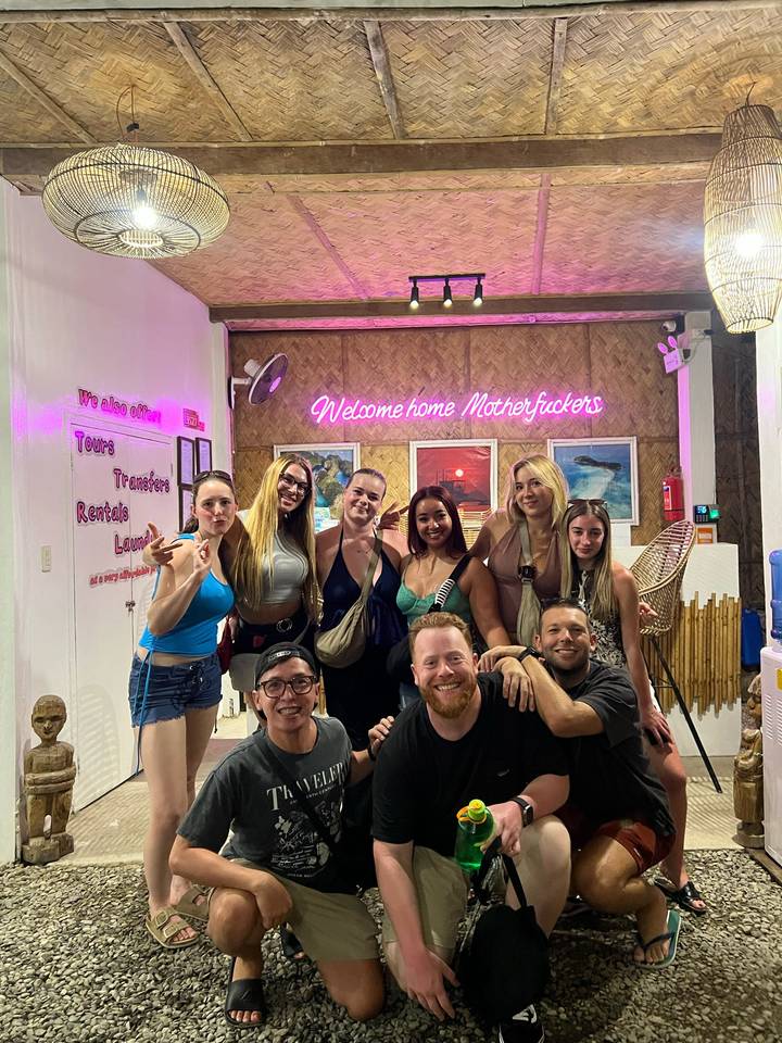 Indoor snapshot of friends posing under a neon welcome sign at a lively bar.