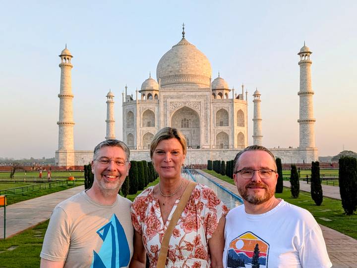 Three travellers smiling in front of the Taj Mahal in warm evening light.