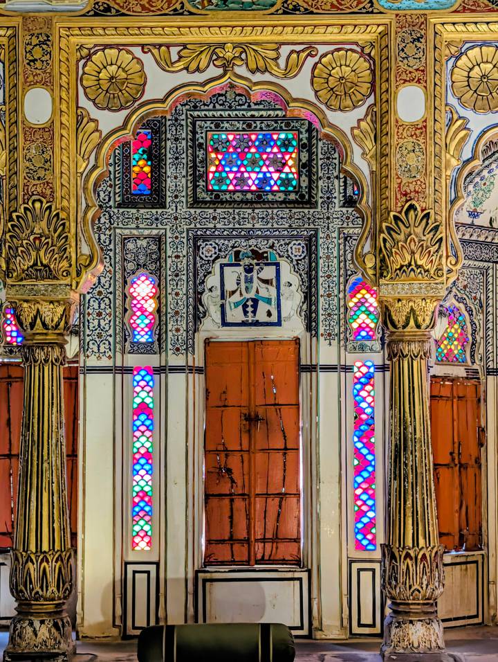 Detailed interior with ornate columns and multicoloured stained-glass panels in an Indian palace.