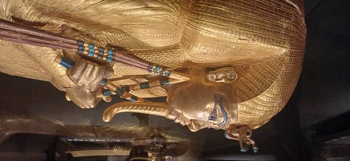 Golden sarcophagus of Tutankhamun with intricate inlay and blue accents displayed under museum lighting