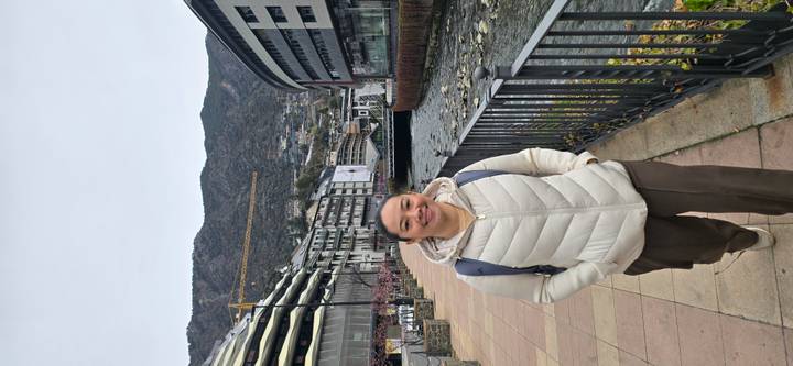 Traveler standing on a riverside promenade with modern buildings and mountains of Andorra behind.
