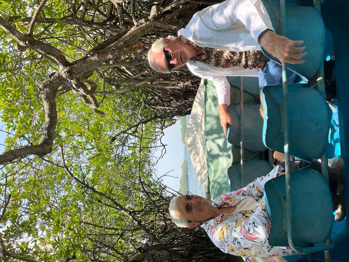 Older couple seated in a small boat gliding through dense mangrove tunnels.