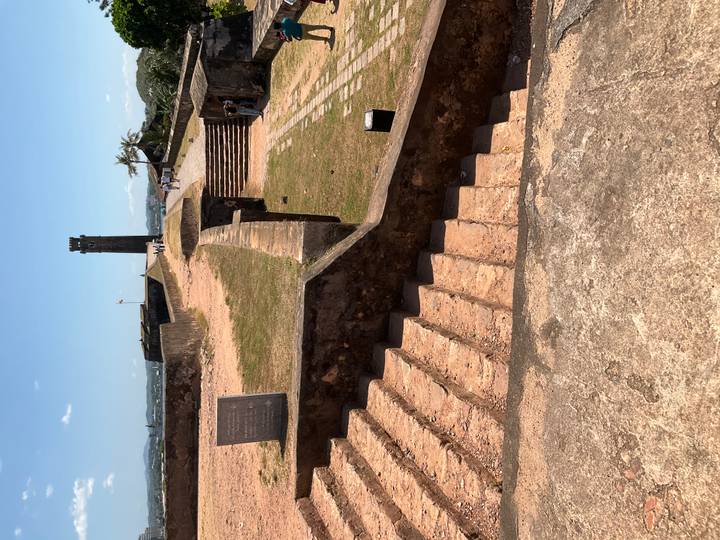 Historic coastal fort ramparts with stone steps and a distant watchtower under clear skies.