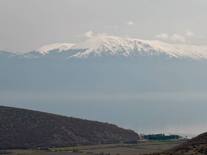 Snow-capped mountain rising above a vast lake with hazy blue tones.