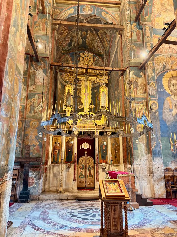 Richly frescoed Orthodox church interior with gilded altar and hanging candle chandelier.