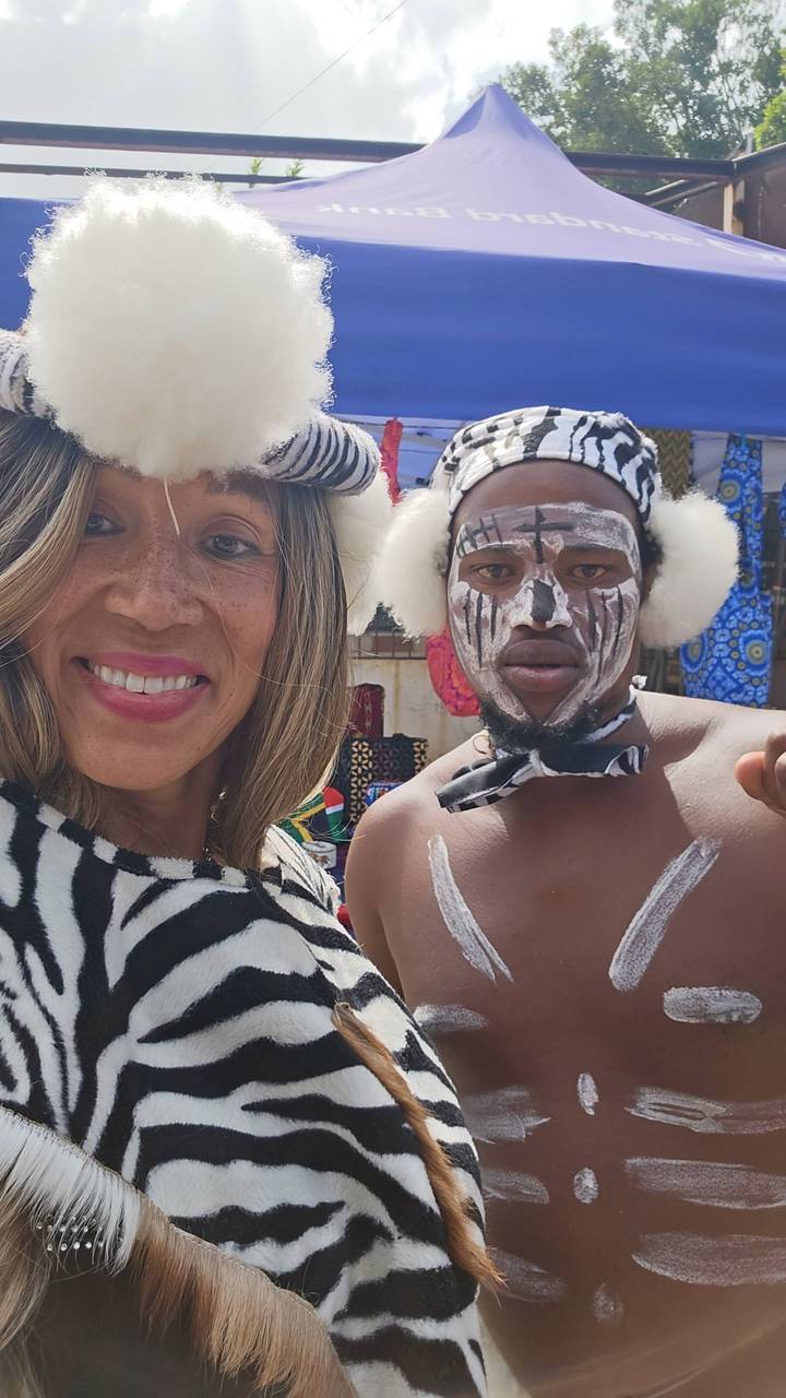 Smiling woman beside traditionally painted performer in open market setting