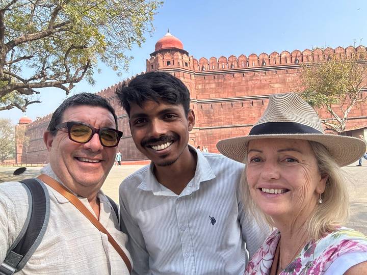 Three smiling travellers taking a selfie in front of the red sandstone walls of Delhi’s Red Fort.