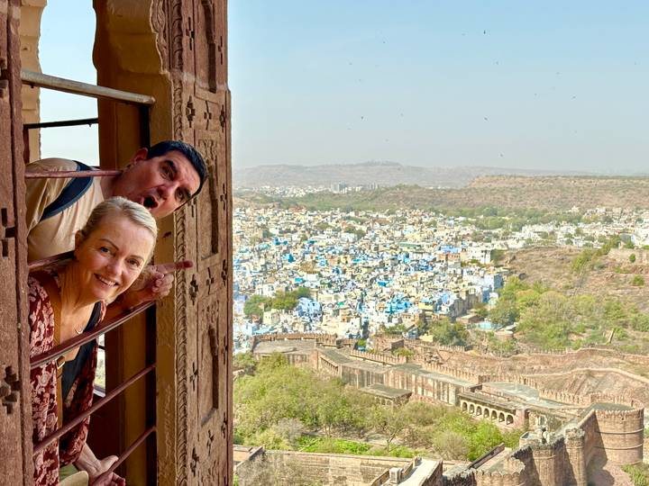 Playful couple leaning from a fortress window overlooking the blue houses of Jodhpur spread across the valley below.