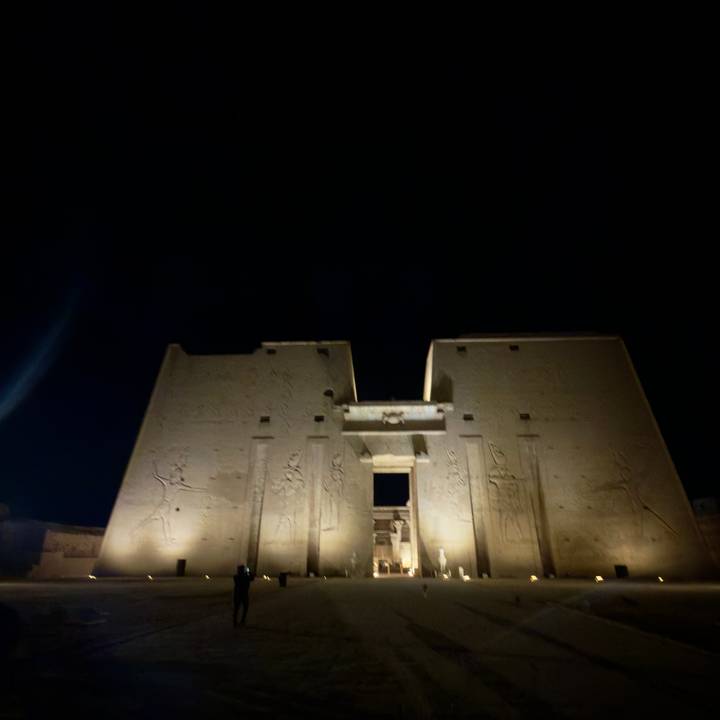 Night view of an Egyptian temple pylon illuminated against a dark sky, image slightly out of focus