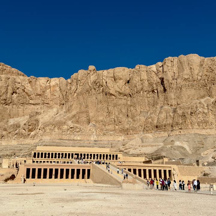 Terraced Temple of Hatshepsut nestles against towering sheer desert cliffs under blue sky