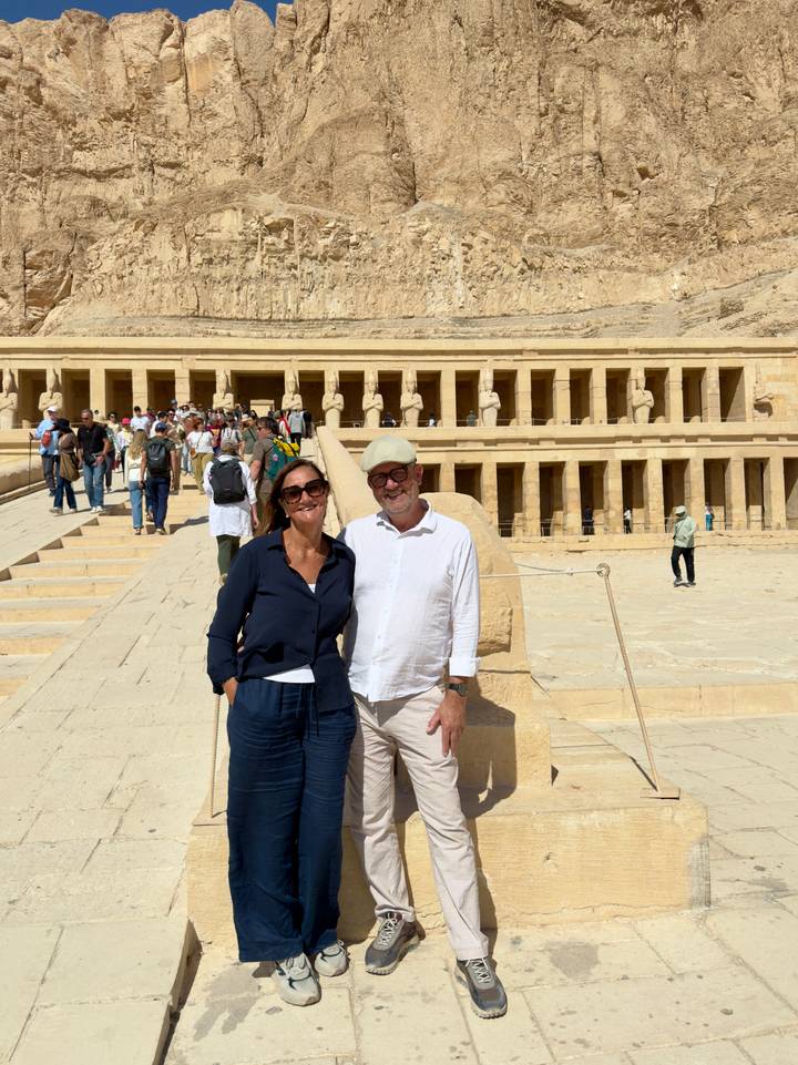 Smiling couple poses in front of the colonnaded Temple of Hatshepsut as tour groups explore behind them
