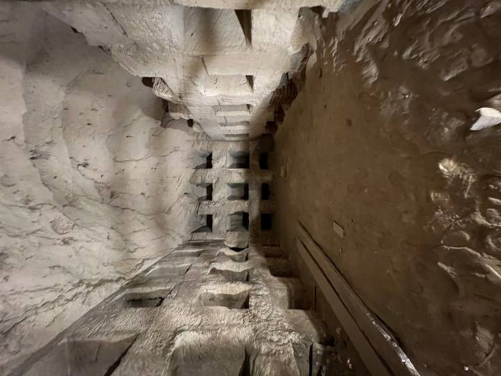 A dark, empty rock-hewn chamber with rows of small alcoves and a rough arched ceiling.