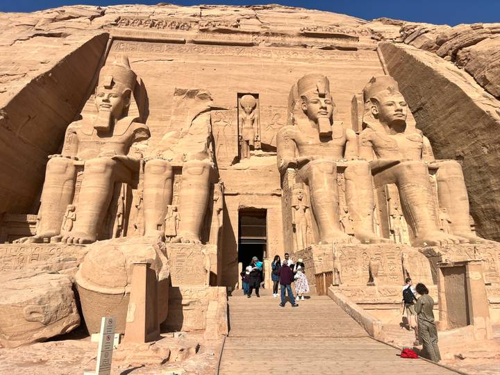 Grand façade of Abu Simbel with four colossal seated statues of Ramses II towering above visitors on the stone steps.