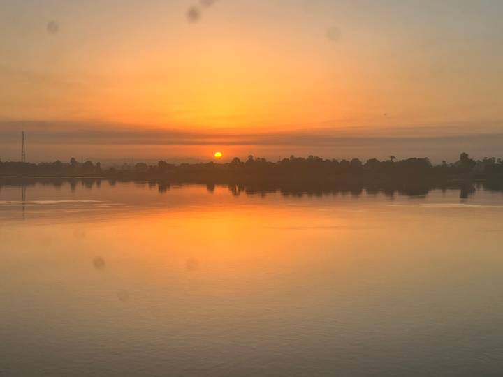 Serene sunset casting orange hues across a calm river reflecting the glowing sky.