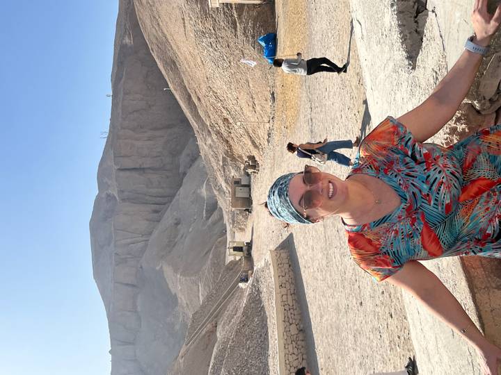 Traveller in patterned headscarf smiling in the sun-baked Valley of the Kings with steep cliffs behind.