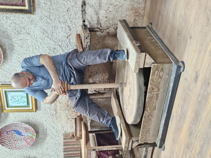 Full view of potter concentrating on shaping clay while seated at kick wheel