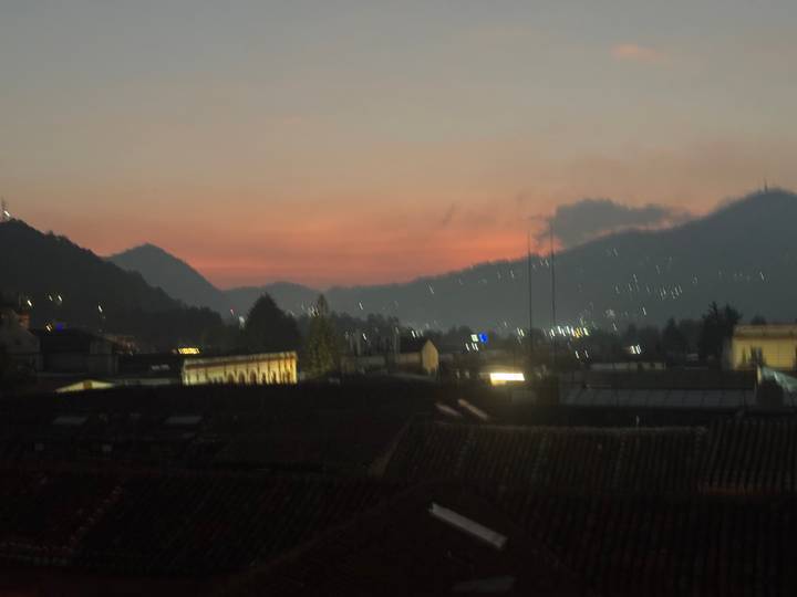 Soft-focus dusk scene of a mountain town with orange-pink sky and scattered lights in the valley.