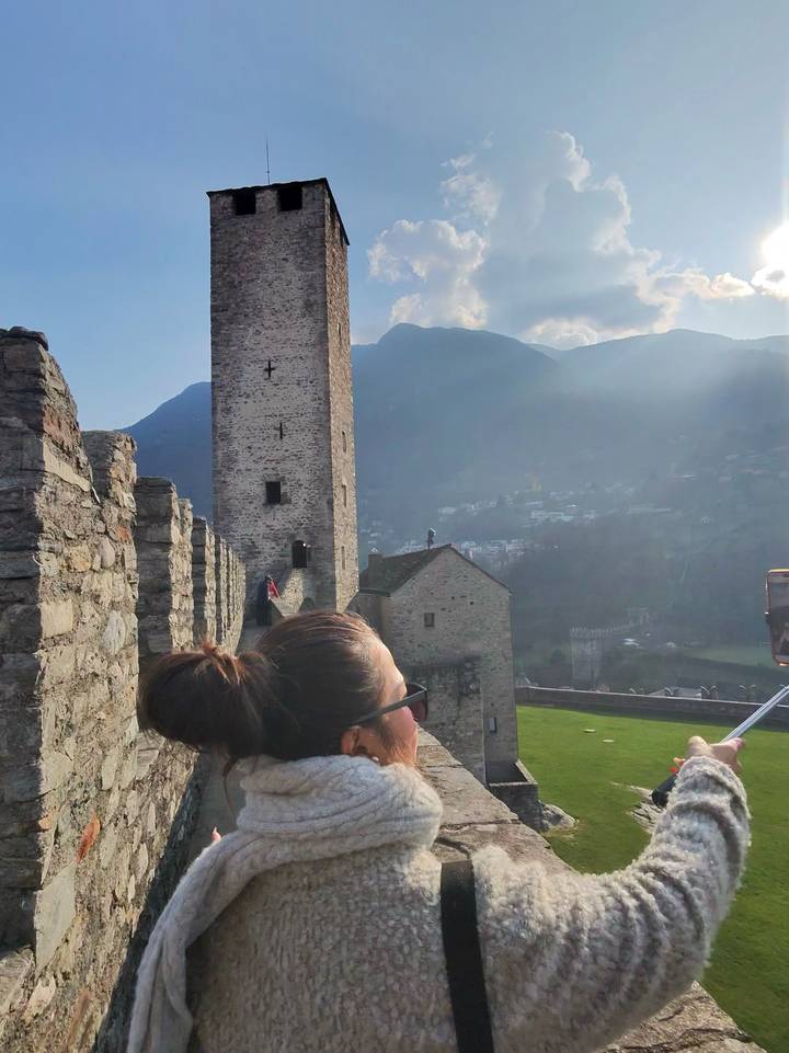 Woman looking out over a medieval stone castle wall with tower and mountains in background