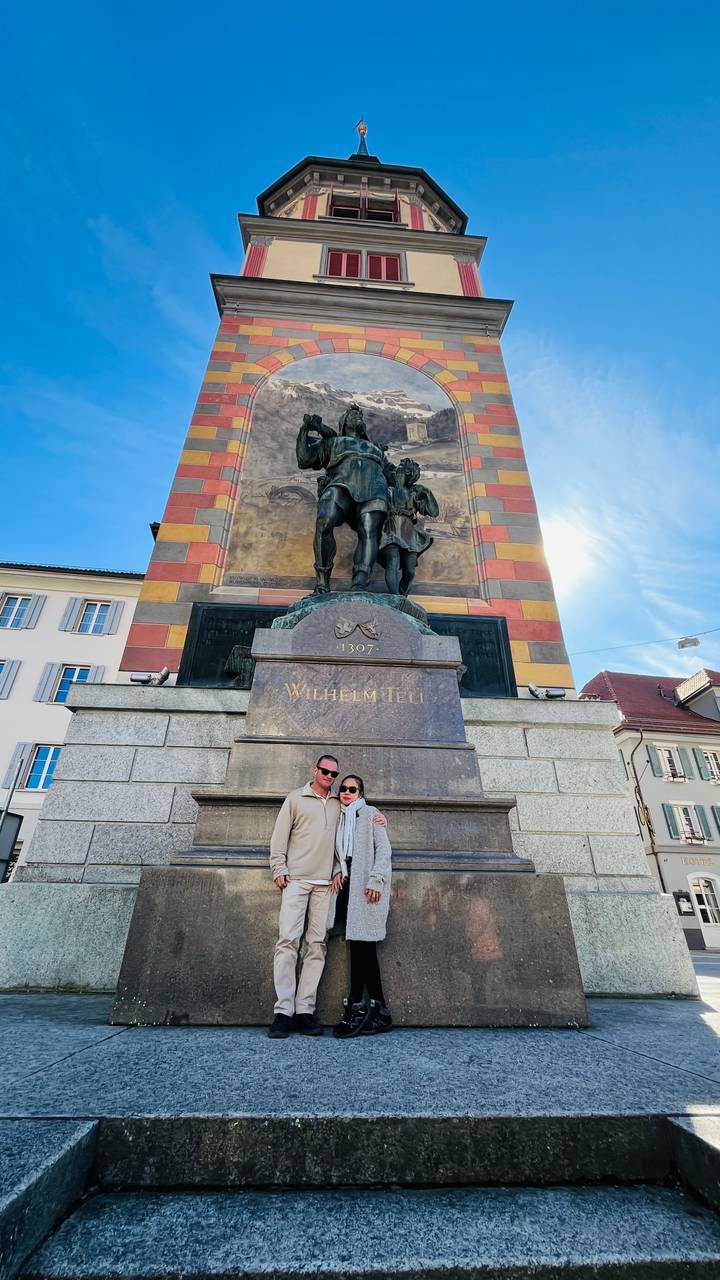 Couple posing at base of the colourful Wilhelm Tell monument in a Swiss town square