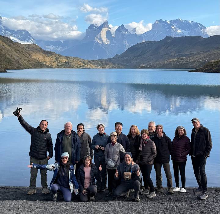 Large group standing by reflective lake with dramatic mountain backdrop in Patagonia