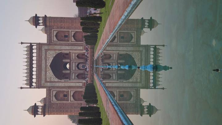 Grand sandstone gateway to the Taj Mahal complex mirrored perfectly in the long reflecting pool at dawn.