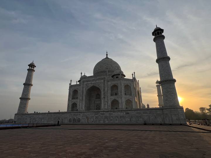 Side silhouette of the Taj Mahal at dawn with soft sun emerging behind a minaret.