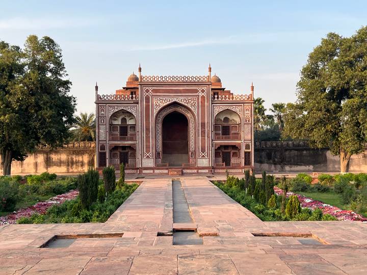 Symmetrical Mughal garden leading to an ornate red and white gateway set amid manicured flowerbeds.