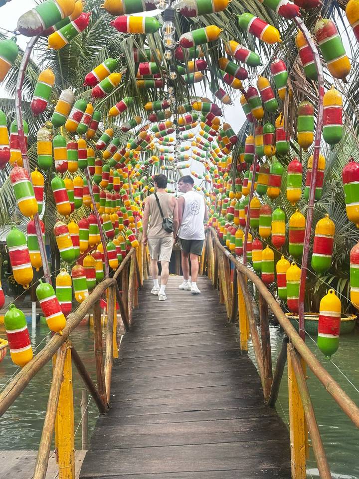 Two travelers walk across a footbridge decorated with rows of colorful buoy floats.