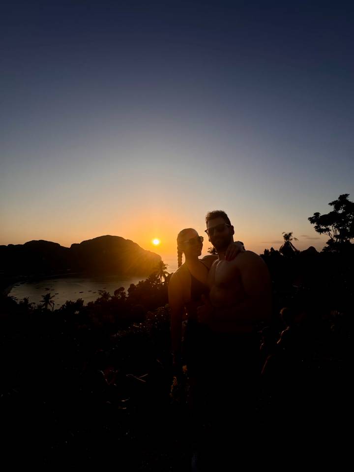 Silhouetted couple posing at sunset viewpoint over island bay