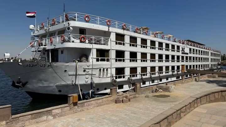 Large multi-deck Nile cruise ship moored at a riverside quay under a clear blue sky