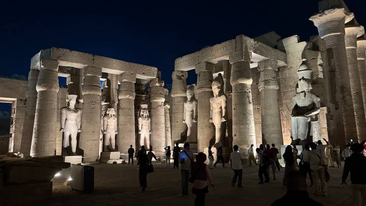 Night illumination of towering columns and statues inside Luxor Temple with tourists walking through