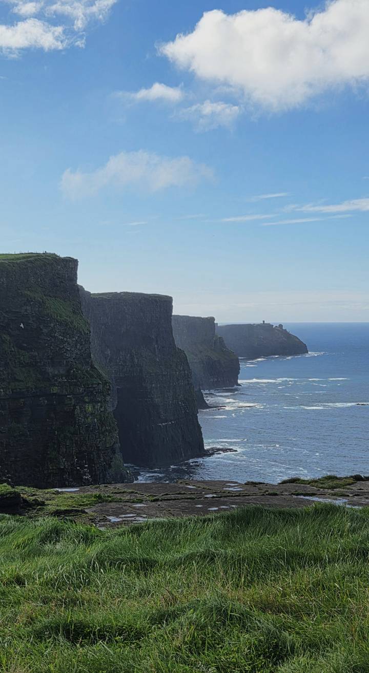 Dramatic vertical sea cliffs rise above the Atlantic Ocean with waves crashing at their base at the Cliffs of Moher.