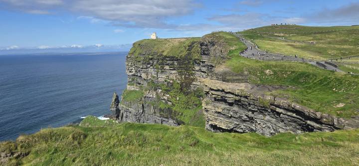 Dramatic view of the Cliffs of Moher with O’Brien’s Tower atop a grassy headland overlooking the Atlantic Ocean.