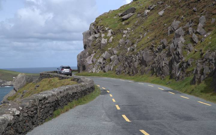 Winding coastal road carved into rocky cliffs with a single parked car and ocean views.