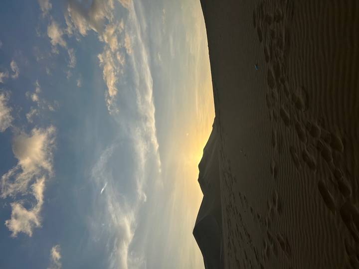 Silhouetted sand dunes at sunset with subtle footprints in the foreground.