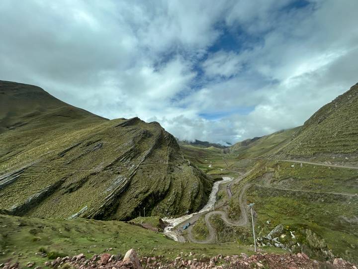 Wide Andean valley with steep green slopes, winding dirt roads and a stream far below.