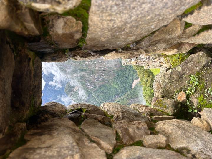 Stone window in an ancient Inca wall framing a lush gorge far below.