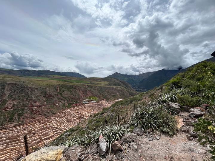 High viewpoint over the salt terraces of Maras carved into a red hillside with stormy skies.