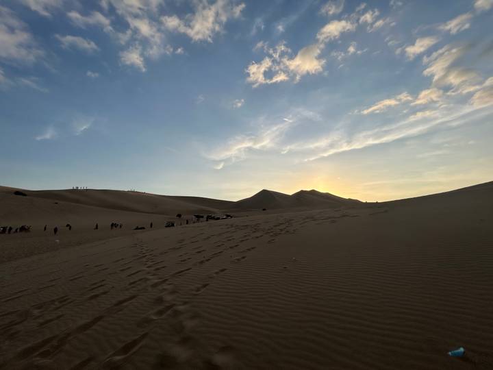 Sunset over desert dunes with footprints and a small group preparing for buggy rides.
