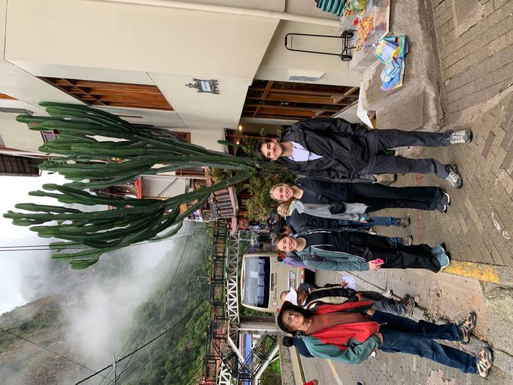 Three young travelers posing on a misty street in Aguas Calientes with tall cactus behind.