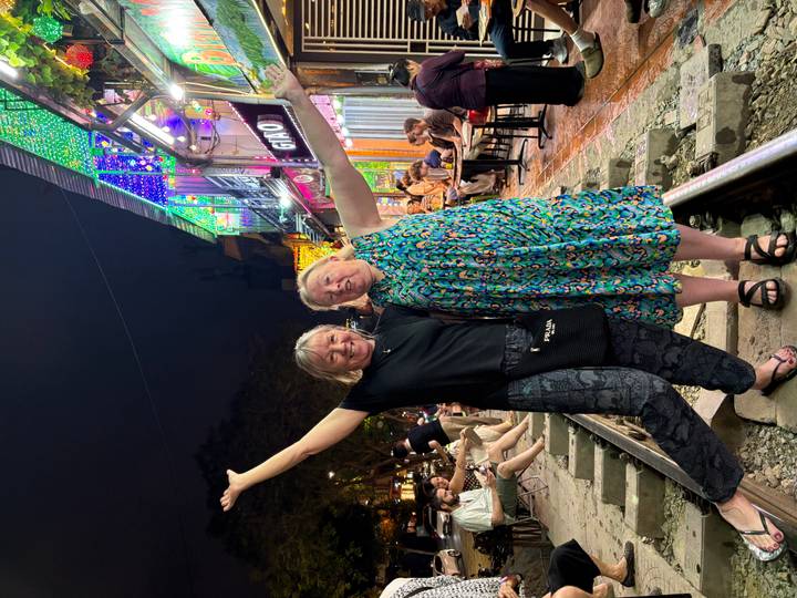 Two women pose happily on Hanoi's train street at night with colorful lights