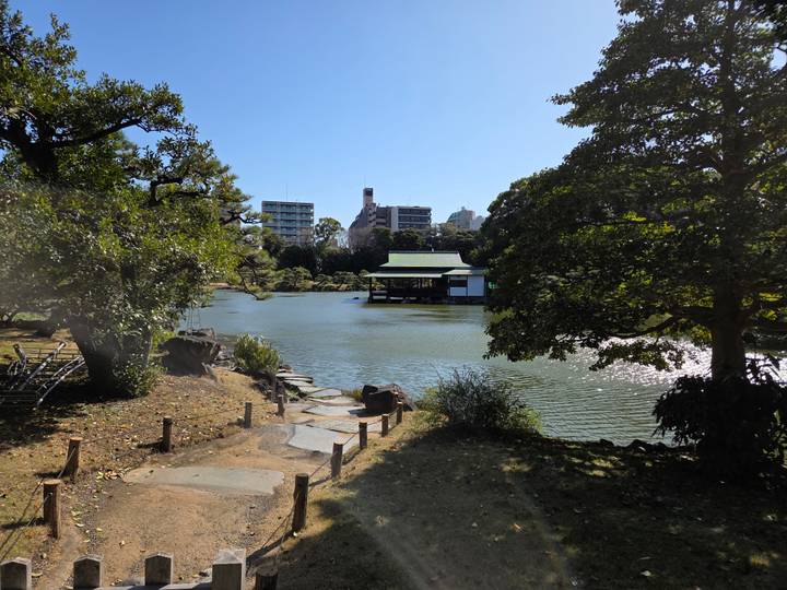 Serene Japanese garden with pond, stepping-stone path and a traditional waterside pavilion surrounded by trees.