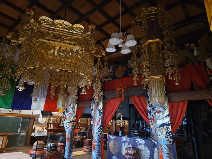 Intricately decorated Buddhist temple interior featuring golden fittings, colorful drapery and carved pillars.