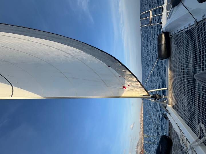White sail billows against a blue sky on a catamaran gliding across the Aegean Sea.