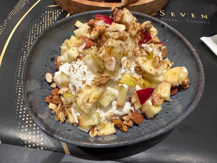 Bowl of creamy Greek yogurt topped with fresh fruit, nuts and honey.
